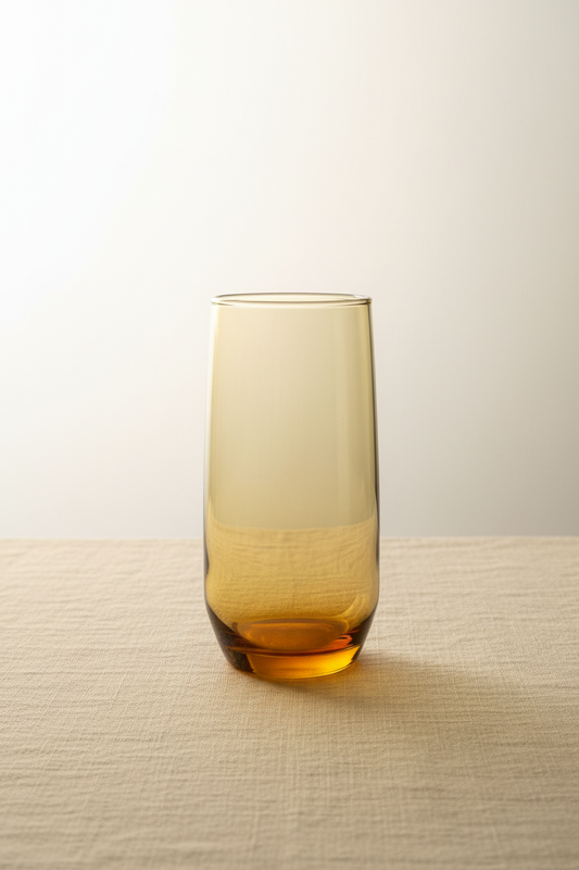 Single vintage mid-century amber glass highball tumbler showing full height straight-sided cylindrical profile with warm honey-amber tinted glass deepening at thick weighted base, neutral background