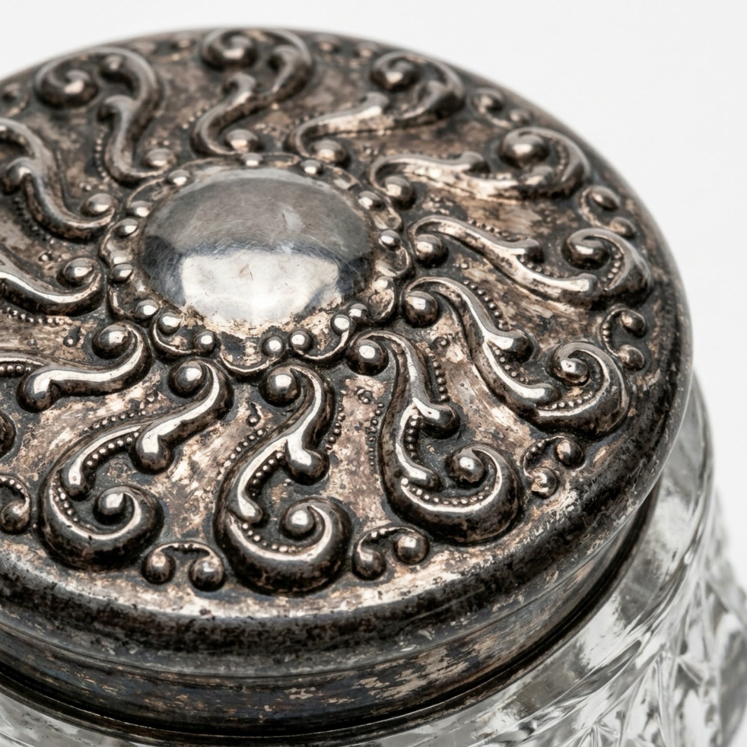 Macro close-up shot of an antique Victorian mixed-metal vanity jar lid featuring a high-relief repoussé scroll and stipple pattern with authentic historical patina.