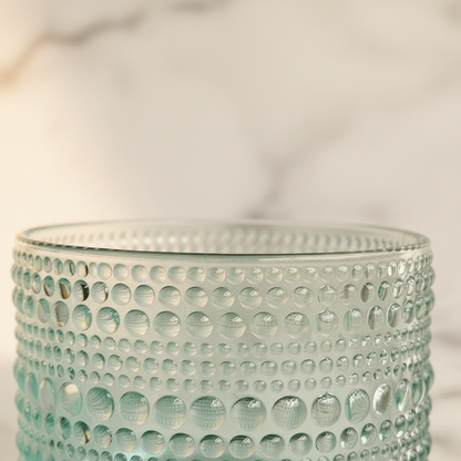 Close-up of aqua hobnail glass body showing raised circular bead pattern and deep teal base against warm backdrop