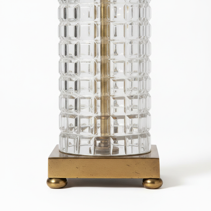 Close-up of vintage table lamp square antique brass plinth with four round ball feet, base of thick clear geometric waffle-grid glass column, light aged brass patina, white background