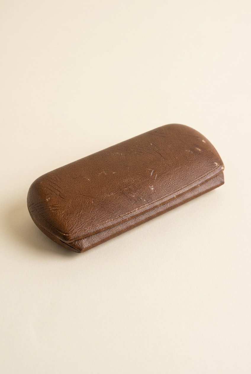 Closed vintage brown eyeglass case on an ivory background