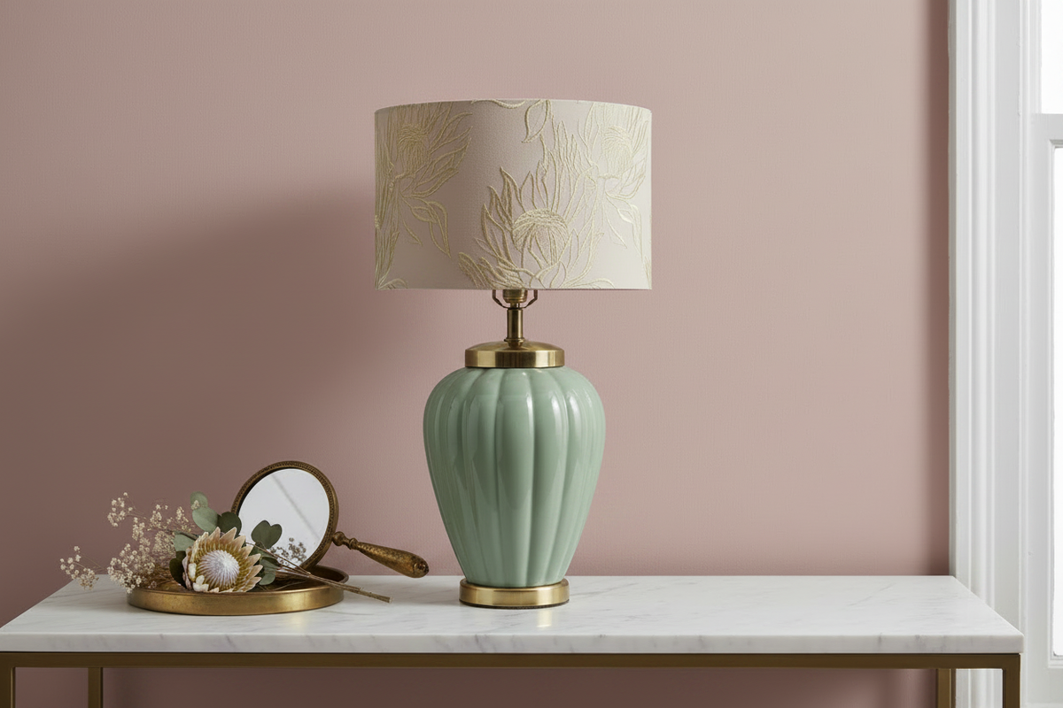 Vintage celadon ceramic table lamp styled on a white marble console table against a dusty rose pink wall with a brass tray, antique hand mirror, and dried protea and eucalyptus botanicals, warm natural window light — shade shown for styling inspiration, not included