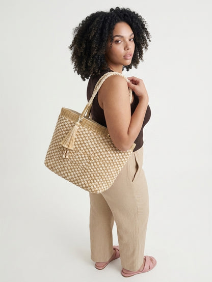 Model looking over her shoulder while carrying the Crosstree Lane woven checkerboard tote by its braided rope handles, styled with a brown tank top and beige linen trousers.