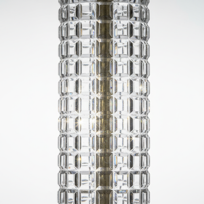 Close-up of vintage clear pressed glass lamp column showing geometric waffle-grid block pattern with rows of faceted rectangular panels, light refracting across crystal-clear glass facets, brass center rod visible through body
