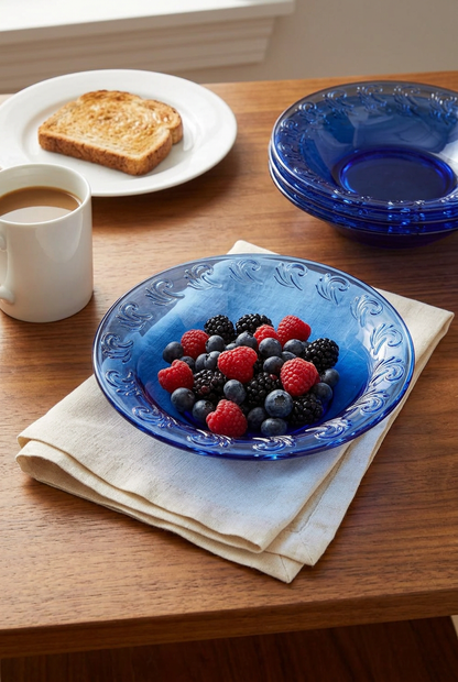 Cobalt blue glass dish holding mixed berries on a linen napkin, with matching dishes, coffee, and toast nearby.
