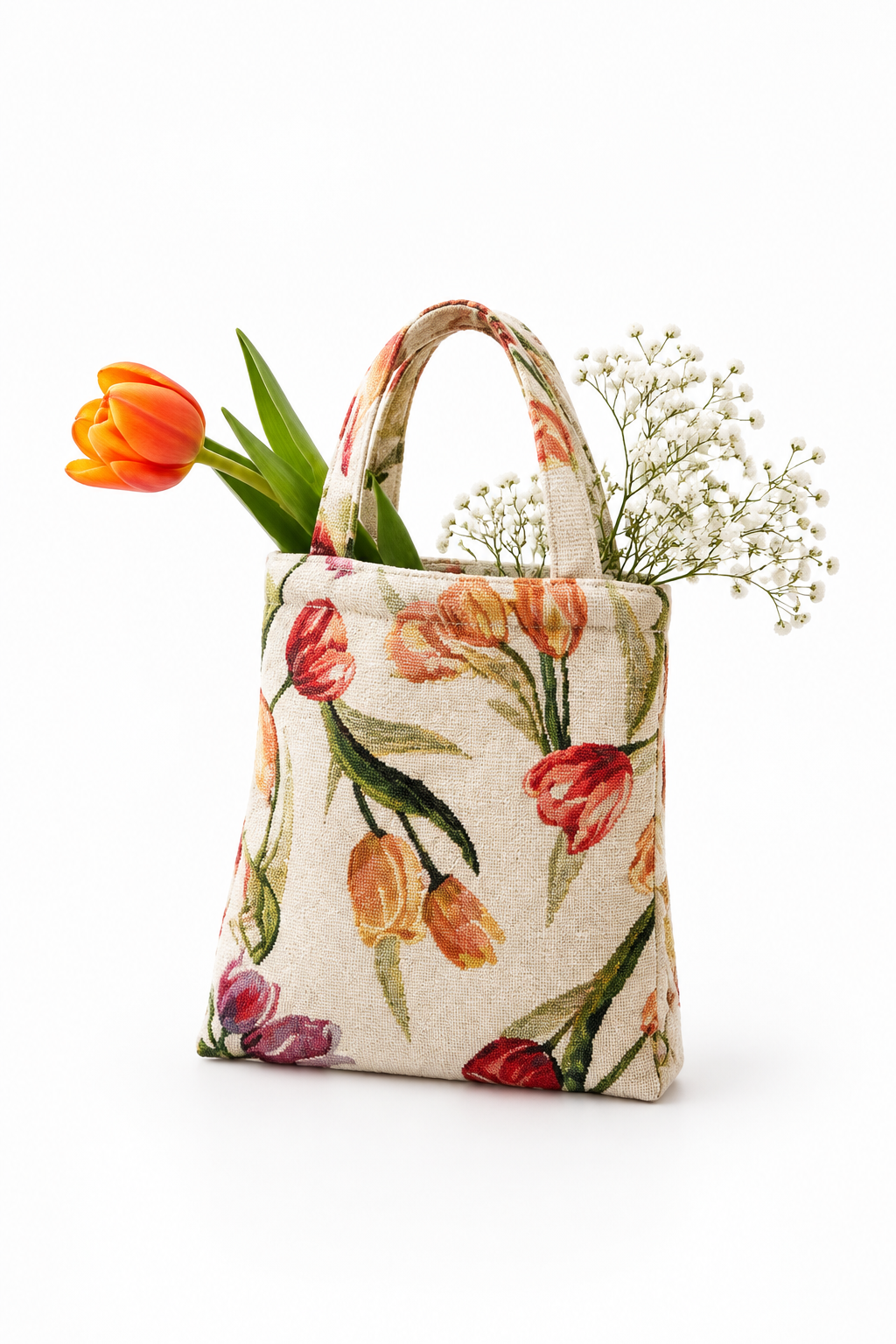 A fabric tote bag with a floral tulip print in orange, red, and purple on a cream background, styled with an orange tulip and baby's breath flowers against a white background.