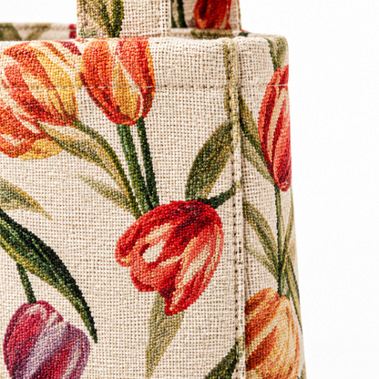 Close-up of a woven tote bag corner featuring a colorful floral tulip pattern on a beige linen-like base, with red, orange, yellow, and purple flowers and green leaves.