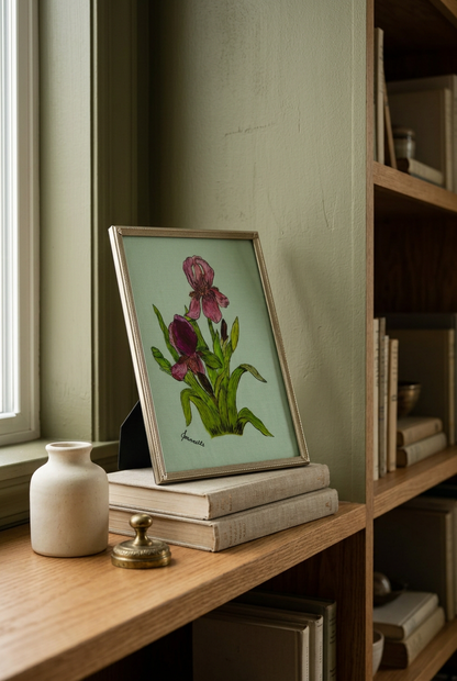 Framed Jeannette iris artwork resting on stacked books beside a cream vase on a wooden bookshelf.