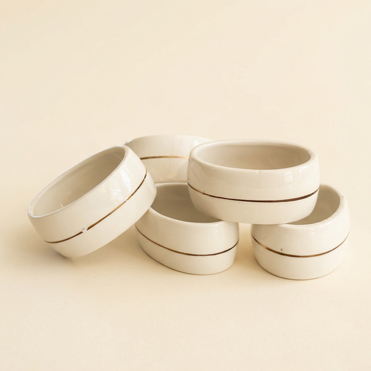 Set of five vintage ivory napkin rings with rounded edges and thin gold-tone center stripes showing small areas of wear.
