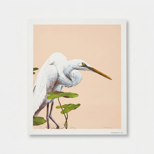 A full-view product shot of an unframed vintage 1980 limited edition wildlife lithograph print by the artist Moriarty, displayed loose on a natural wood surface. The artwork depicts a majestic white Great Egret bird standing gracefully in rippling water among green lily pads. The background is a solid, clean, minimalist warm neutral taupe and sand color. The print is in mint condition with sharp corners and bright white paper borders.