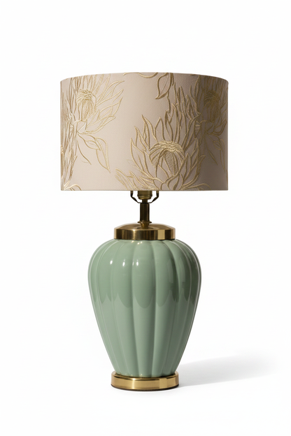 Vintage 1980s celadon glazed ceramic table lamp base in lobed melon urn form with polished brass shoulder collar and brass plinth, shown with embroidered cream botanical drum shade for scale on white background — shade not included