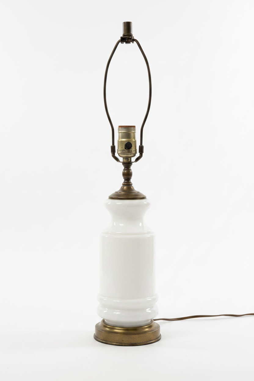 Vintage 1960s opaque white milk glass table lamp base shown without shade, stepped urn-to-cylinder profile with raised ring detail at lower body, antiqued brass shoulder cap and large circular brass plinth base with aged patina, brass harp and E26 turn-knob socket visible, brown cord, white background

