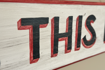 Angled close-up of the black and red 3D block lettering on a textured, white-painted wood grain background.