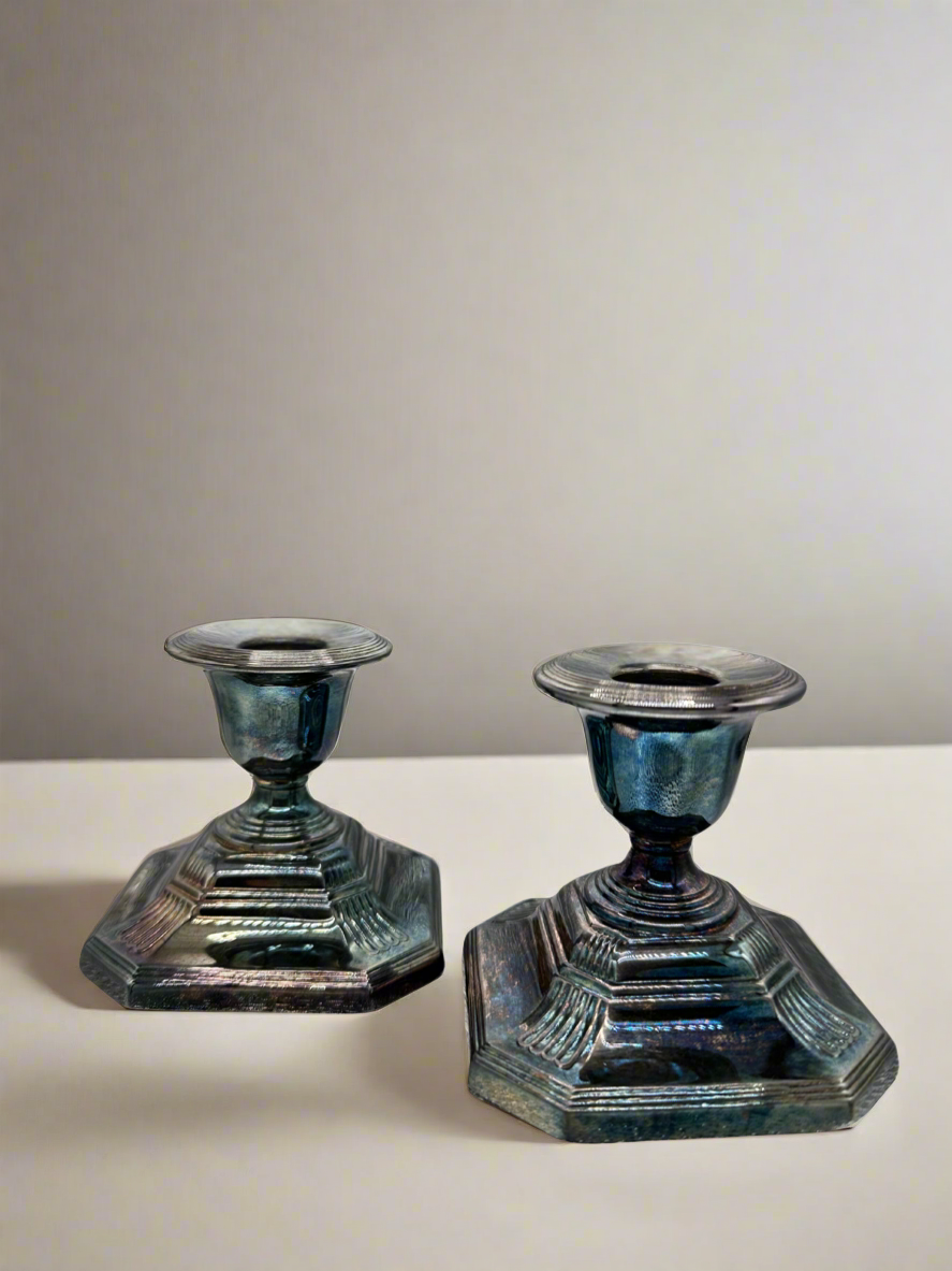 Two iridescent silver candle holders on a white surface with a gray background