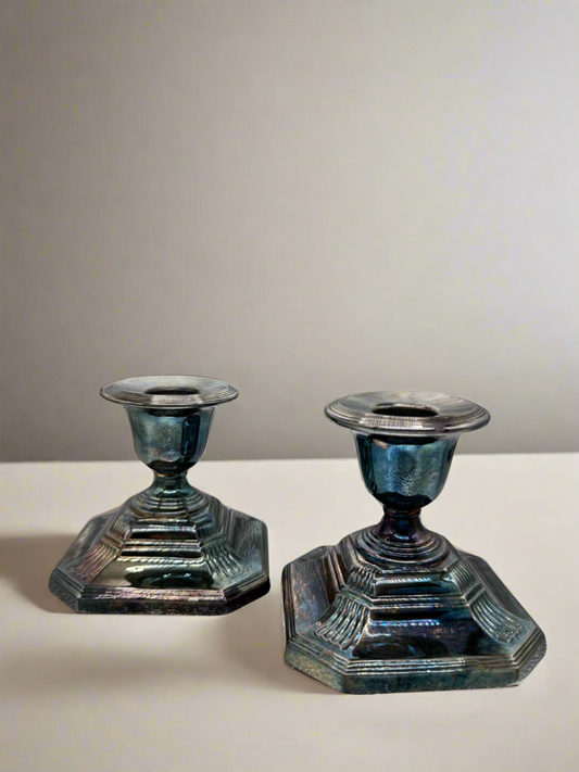 Two iridescent silver candle holders on a white surface with a gray background