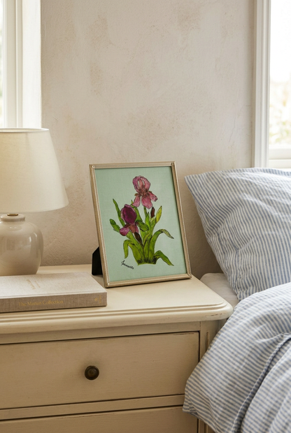  Framed pink and purple iris artwork on a cream nightstand beside a ceramic lamp and blue-striped bedding.