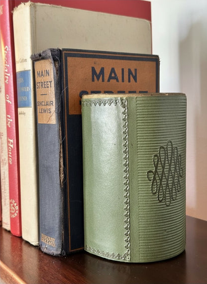 Detailed macro shot of a weighted sage green library bookend displaying the textured difference between the smooth, hand-tooled look front flap and the tightly ribbed curved side panel.