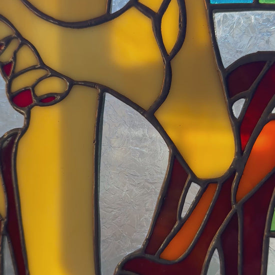 Colorful stained glass art featuring high-heeled shoes in red and orange shades, accented with yellow and green.