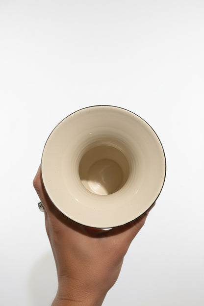 A top-down view of a hand holding the flared rim of a vintage ceramic vase against a white background, looking down into its smooth, glossy cream-colored interior.