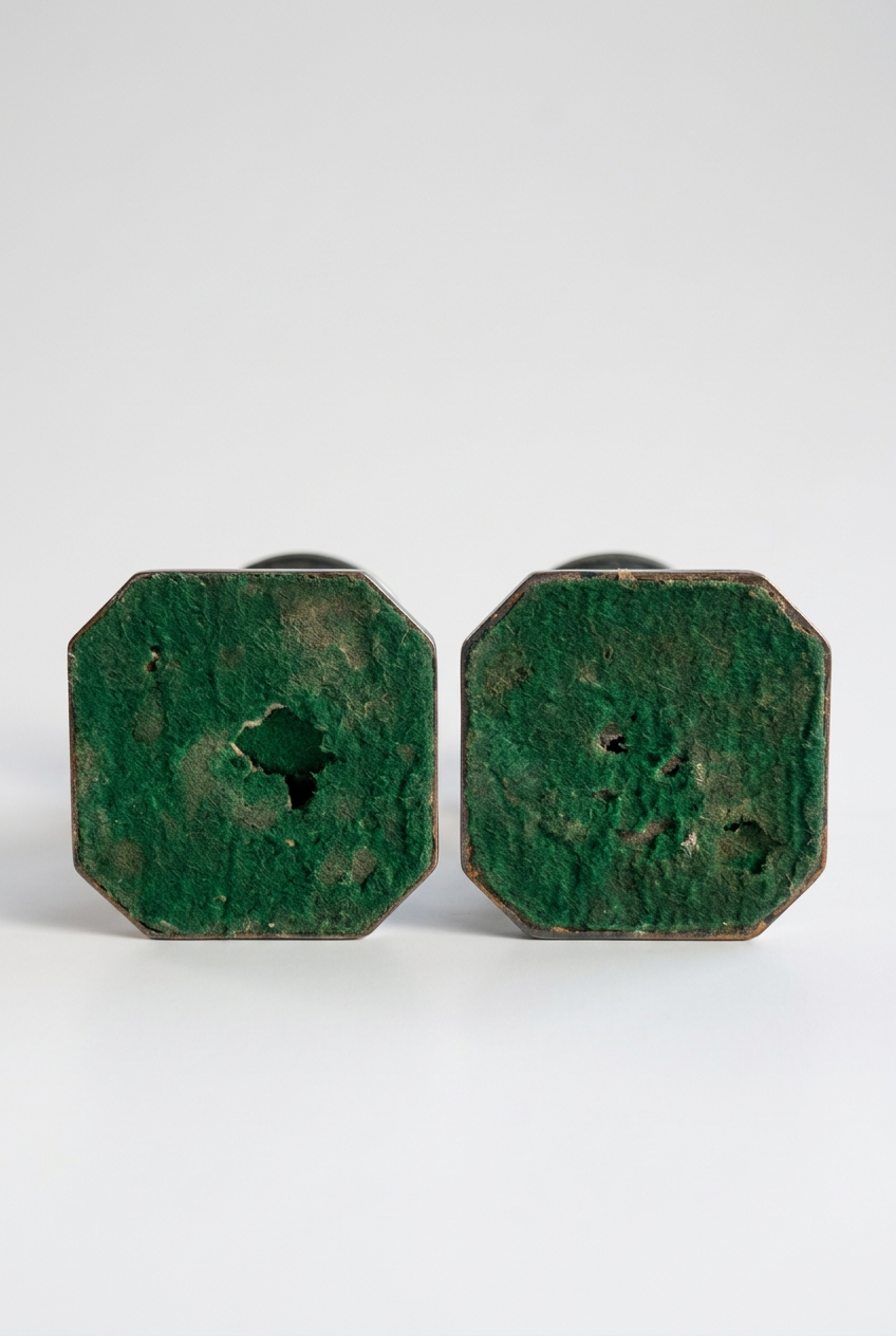 Undersides of two octagonal candlestick bases with green felt coverings showing worn patches, frayed areas, and small holes.