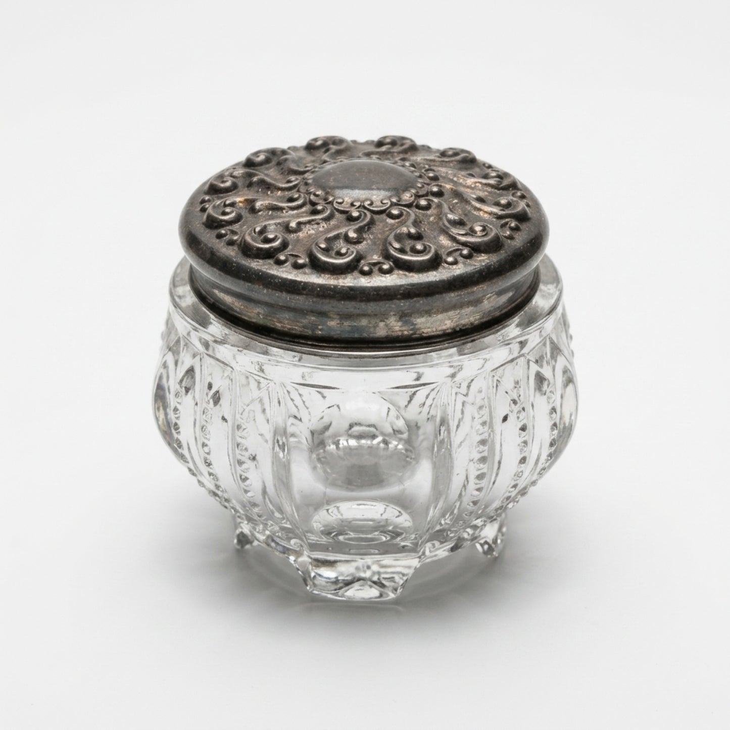 Three-quarter top view of clear pumpkin-shaped antique glass dresser trinket box with a dark embossed metal slip-on lid.