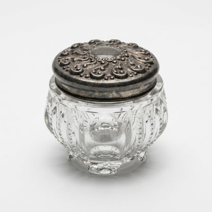 Three-quarter top view of clear pumpkin-shaped antique glass dresser trinket box with a dark embossed metal slip-on lid.