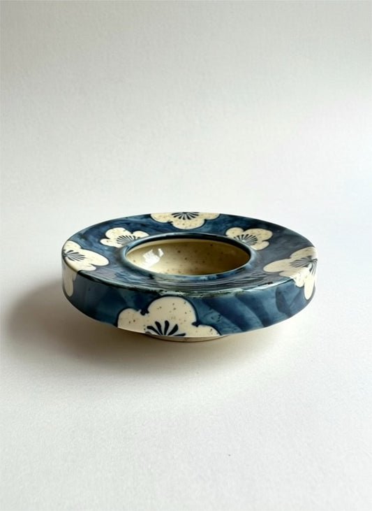 Ceramic plant water retention dish with blue and white design on a light gray background