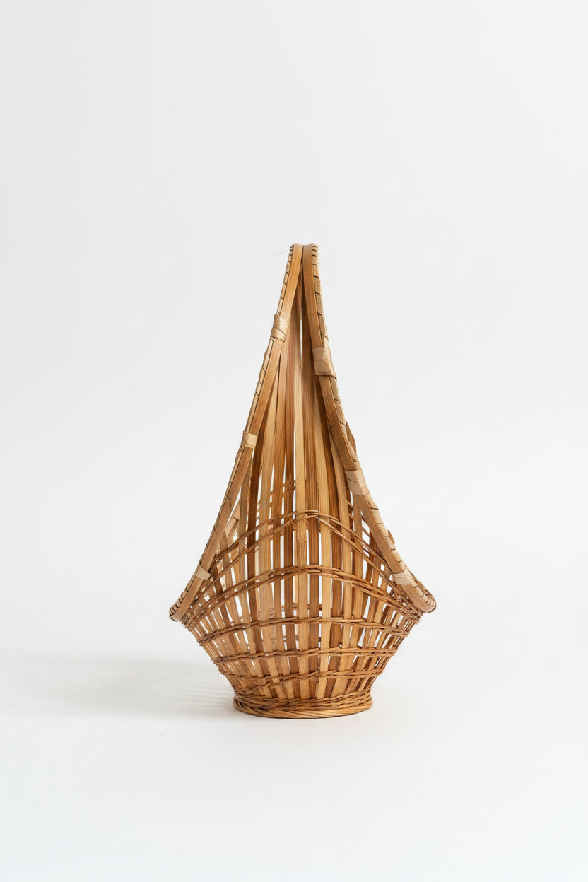 A top-down, side-angled view of a vintage mid-century modern split-bamboo basket showcasing its slender, elongated boat-shaped silhouette against a clean white background. This perspective highlights the concentric circle pattern of the airy, open-work grid radiating from a tightly woven starburst center, paired with a distinct wrapped bamboo hoop handle running along the top edge, as seen in D574C52A-F876-4662-A9CA-9EC4412F431A.jpg.