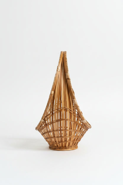 A top-down, side-angled view of a vintage mid-century modern split-bamboo basket showcasing its slender, elongated boat-shaped silhouette against a clean white background. This perspective highlights the concentric circle pattern of the airy, open-work grid radiating from a tightly woven starburst center, paired with a distinct wrapped bamboo hoop handle running along the top edge, as seen in D574C52A-F876-4662-A9CA-9EC4412F431A.jpg.