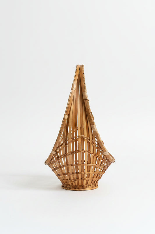 A top-down, side-angled view of a vintage mid-century modern split-bamboo basket showcasing its slender, elongated boat-shaped silhouette against a clean white background. This perspective highlights the concentric circle pattern of the airy, open-work grid radiating from a tightly woven starburst center, paired with a distinct wrapped bamboo hoop handle running along the top edge, as seen in D574C52A-F876-4662-A9CA-9EC4412F431A.jpg.